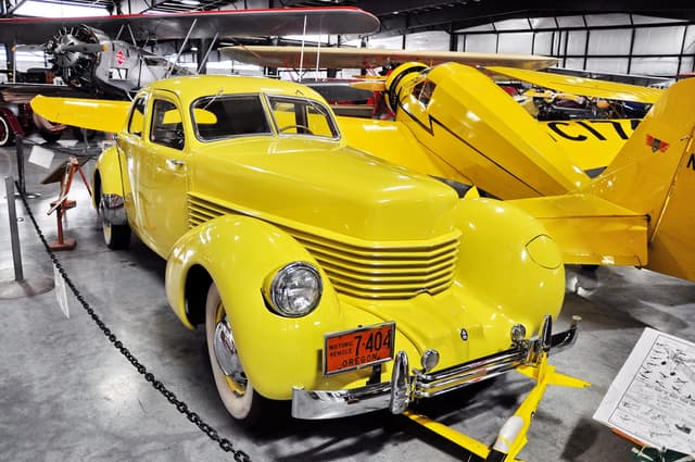 A vintage, yellow car parked next to a vintage, yellow aircraft.